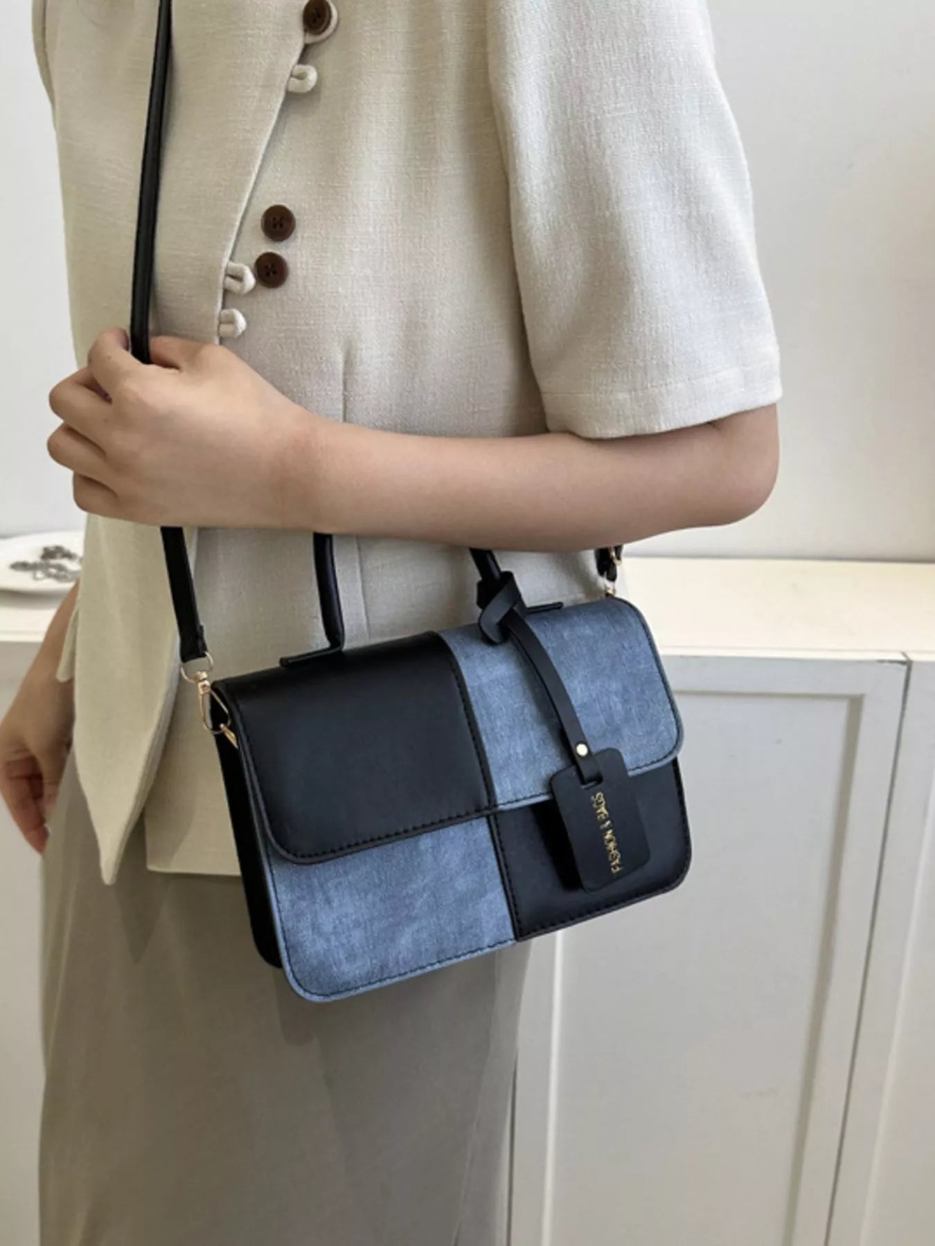 Person holding a blue and black handbag with a neutral background