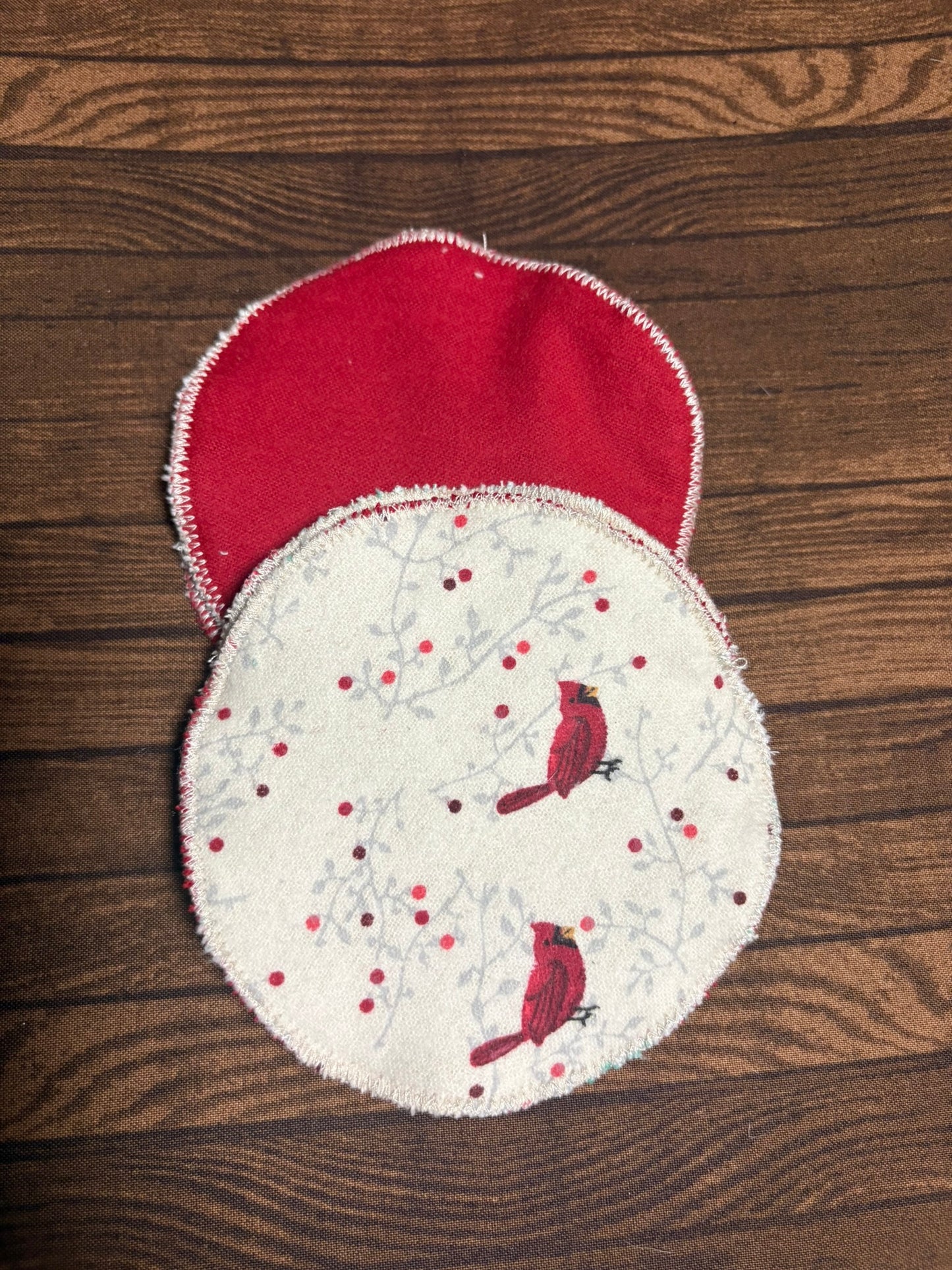 Two fabric makeup pad removers with red bird designs on a wooden surface