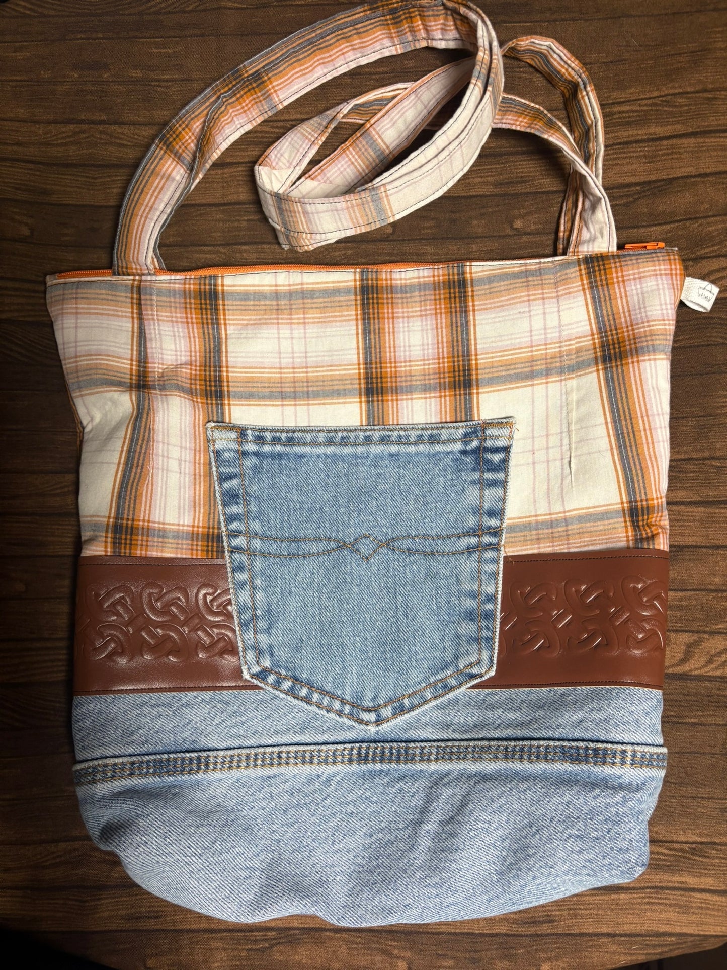 Handbag made from repurposed denim with plaid pattern and brown leather accents on a wooden surface