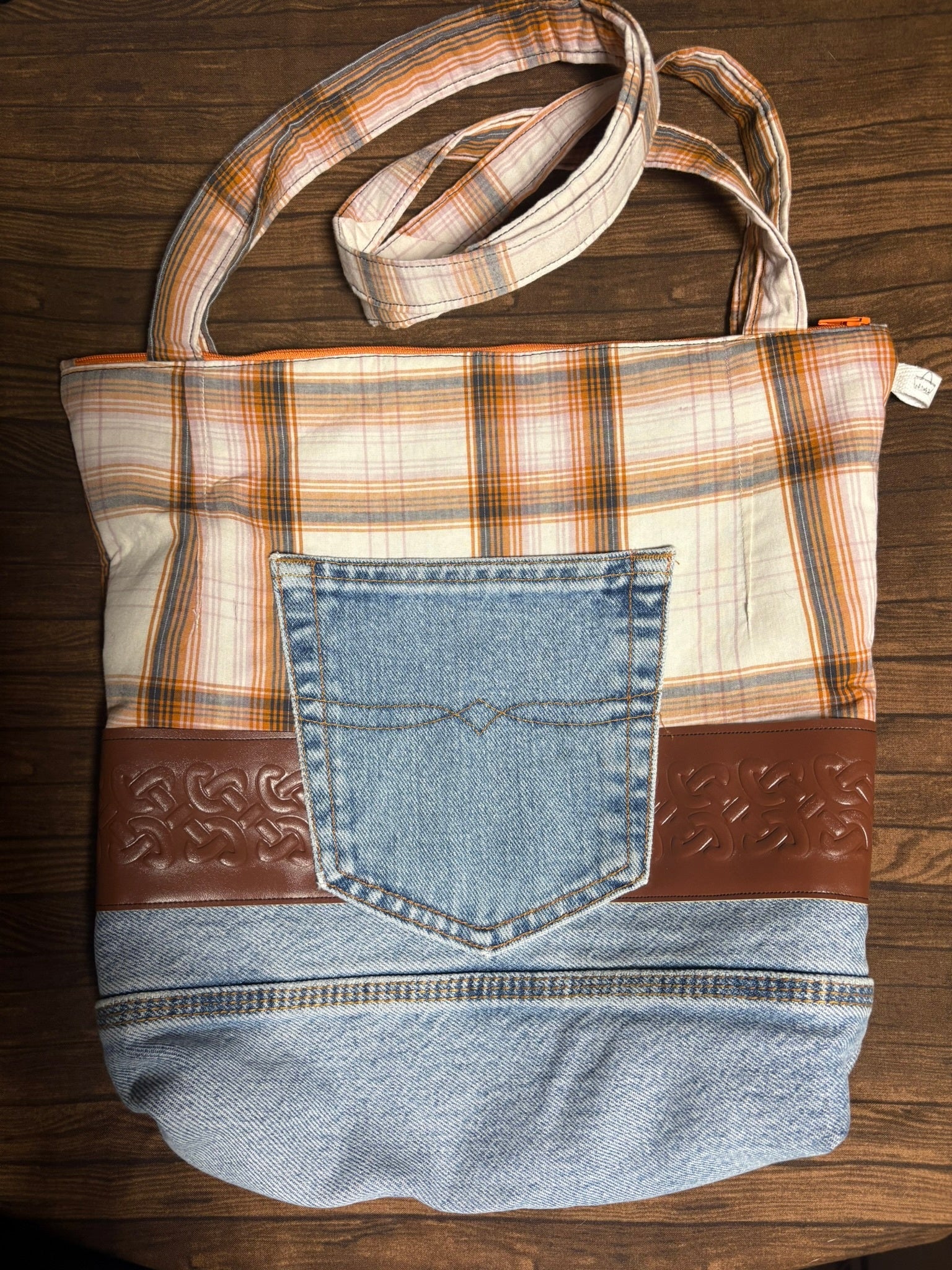 Handbag made from repurposed denim with plaid pattern and brown leather accents on a wooden surface