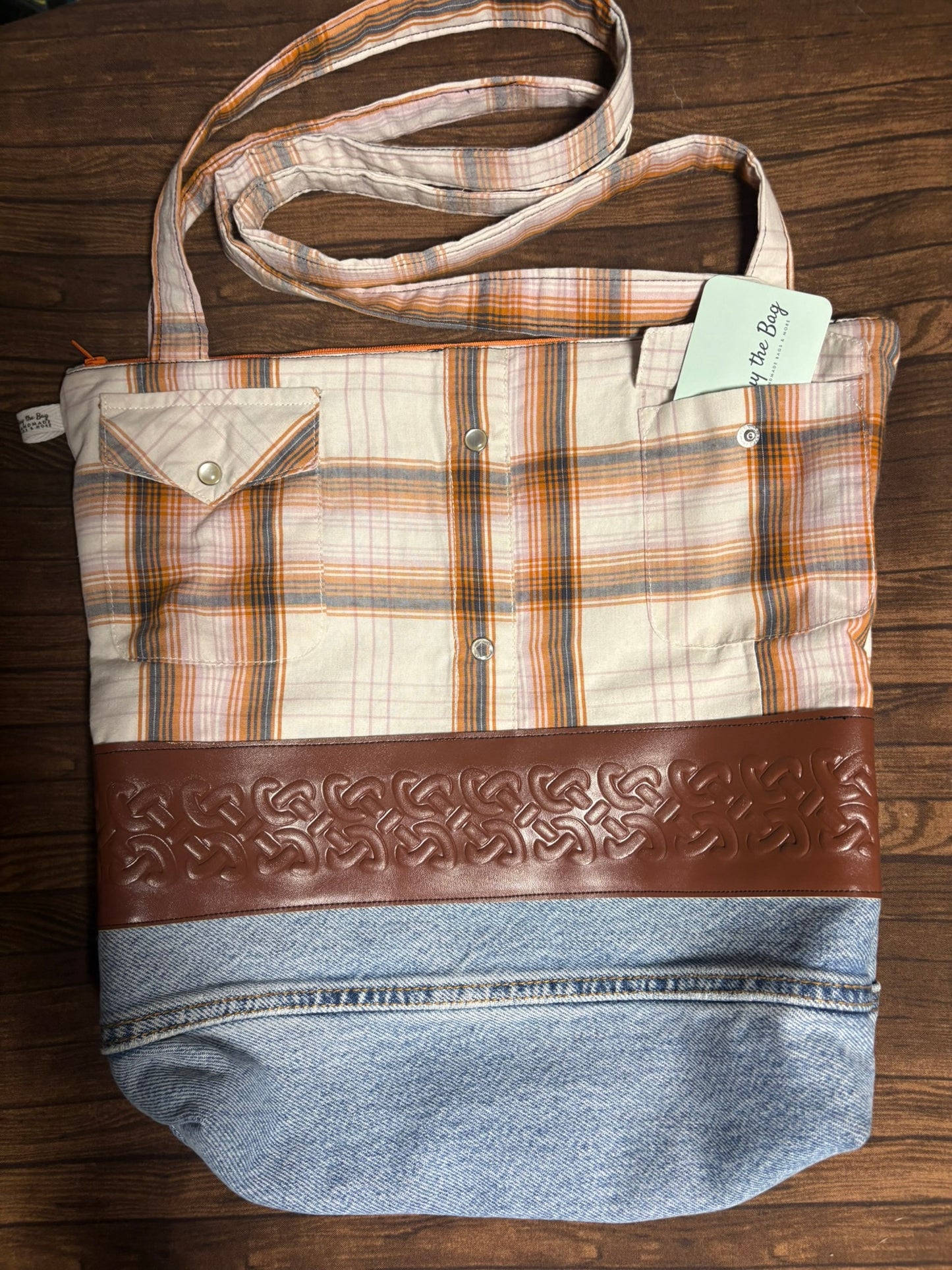 Plaid bag with denim bottom and brown leather strap on a wooden surface