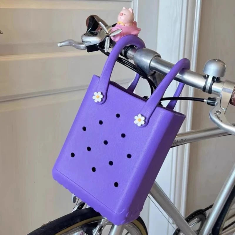 Purple bicycle basket with floral decorations attached to a bike handlebar.